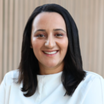 Portrait of a smiling woman with shoulder-length black hair wearing a white blouse, against a neutral background.