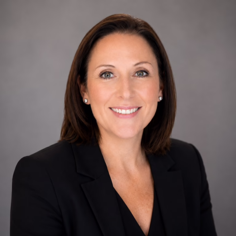 Professional headshot of a smiling woman in a black blazer against a neutral gray backdrop, businesslike and approachable.