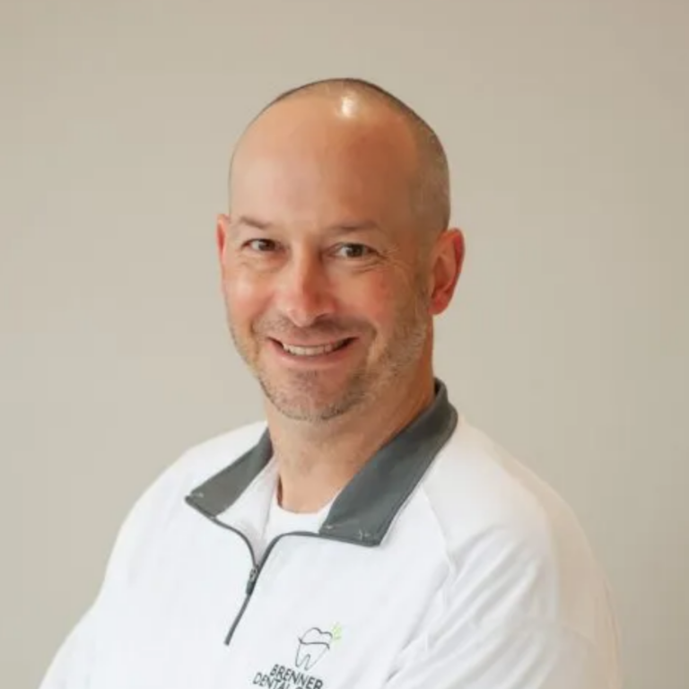 Smiling man in a white dental coat, posed for a professional headshot.