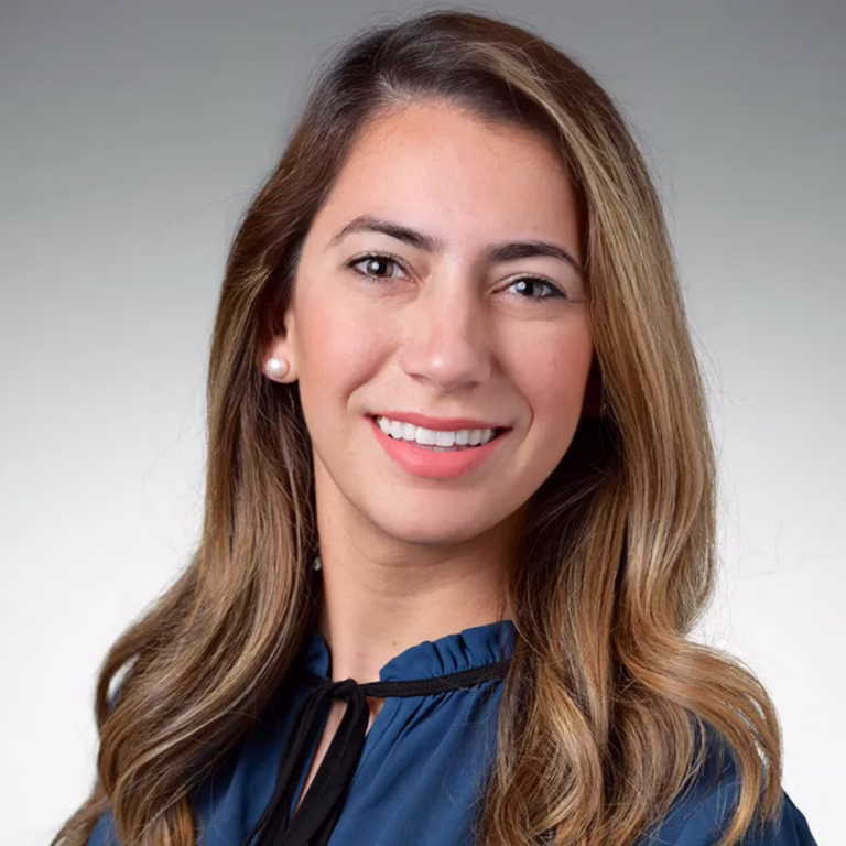 Portrait of a smiling woman with long light brown hair, wearing a blue blouse, against a neutral gradient background.