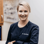 Smiling female healthcare professional in navy scrubs with 'Dr. Amy Connor' embroidered on the chest.