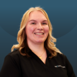 Smiling woman with blonde hair wearing a black polo shirt, posing against a blue gradient background.