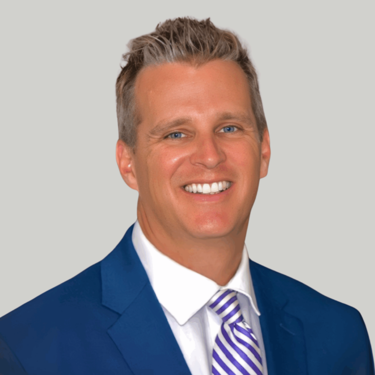 Professional headshot of a smiling man in a blue suit and striped purple tie against a light gray background.