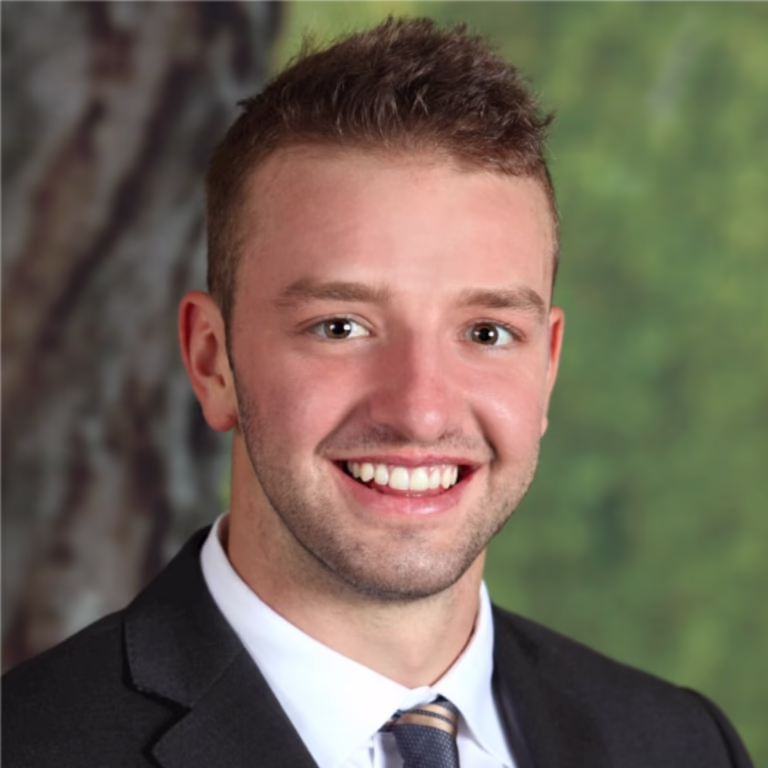 Smiling man in a suit and tie, posing for a professional headshot with a green, blurred background.