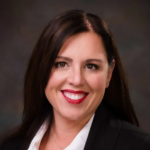 Smiling woman in a black blazer and white blouse, professional headshot against a neutral background.