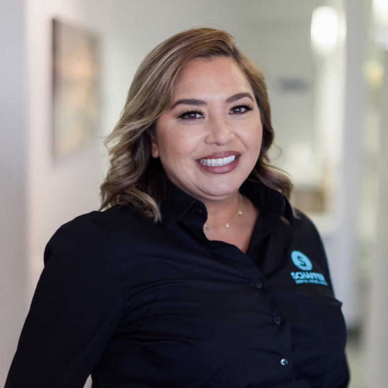Smiling woman in a black button-down shirt with a teal logo on the chest, standing in a bright hallway (professional portrait).