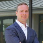Professional man in a navy windowpane suit smiling with arms crossed outdoors.