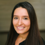 Portrait of a smiling woman with long dark hair looking at the camera, neutral background.