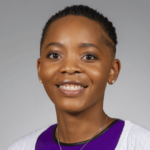 Smiling woman with short natural hair wearing a purple top and white cardigan, against a gray background (head-and-shoulders portrait).