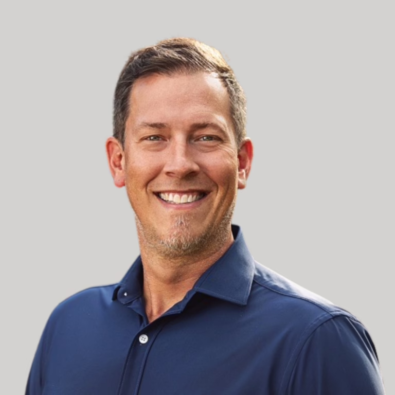 Head-and-shoulders portrait of a smiling man in a navy blue shirt against a neutral gray background.