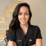 Smiling female healthcare professional in black scrubs with arms crossed, in a clinic setting.