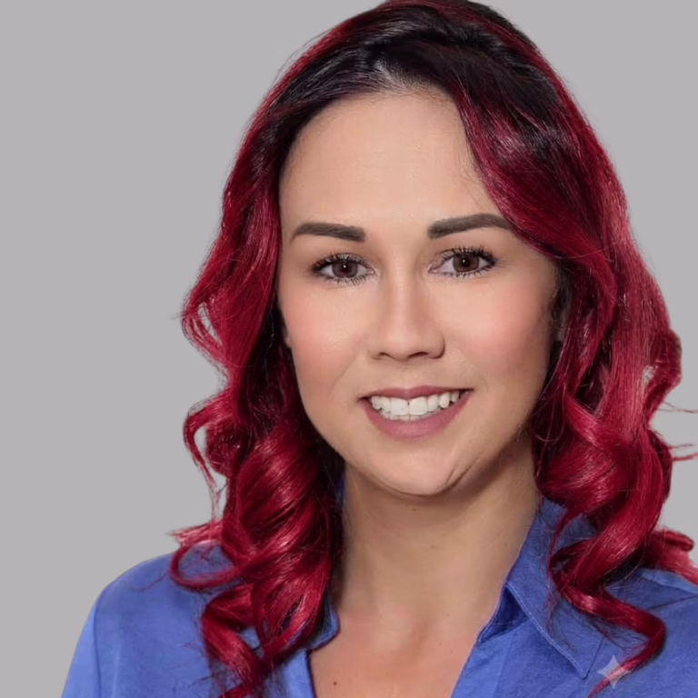Portrait of a woman with red wavy hair wearing a blue shirt, smiling against a gray background.