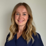 Portrait of a smiling woman with shoulder-length blonde hair in a navy blouse against a light background.