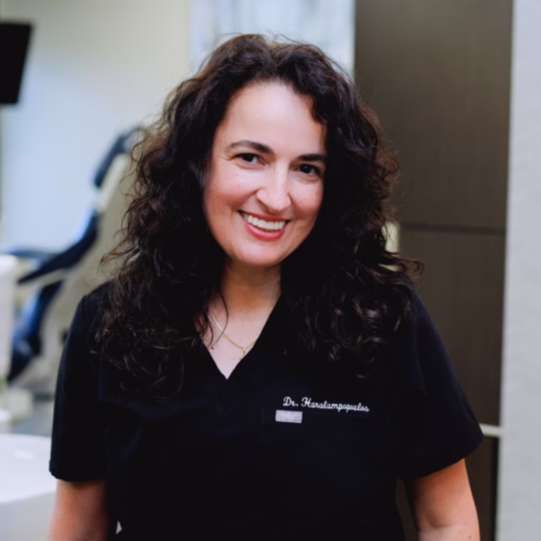 Smiling woman in black scrubs with a name badge, standing in a clinic setting.