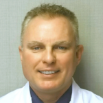 Portrait of a smiling male doctor in a white coat, facing the camera in a neutral setting