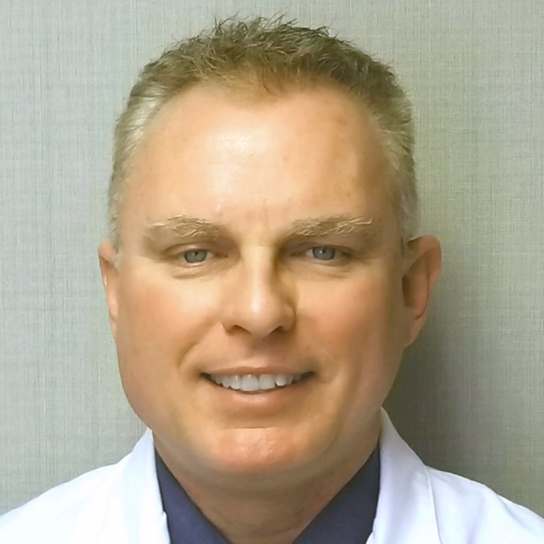 Portrait of a smiling male doctor in a white coat, facing the camera in a neutral setting