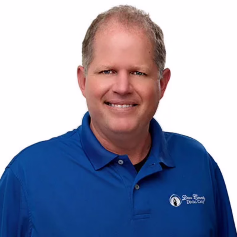 Smiling man wearing a blue polo shirt with a chest logo, against a white background.