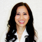 Smiling woman with long dark hair wearing a white blouse, posing against a sparkly backdrop.