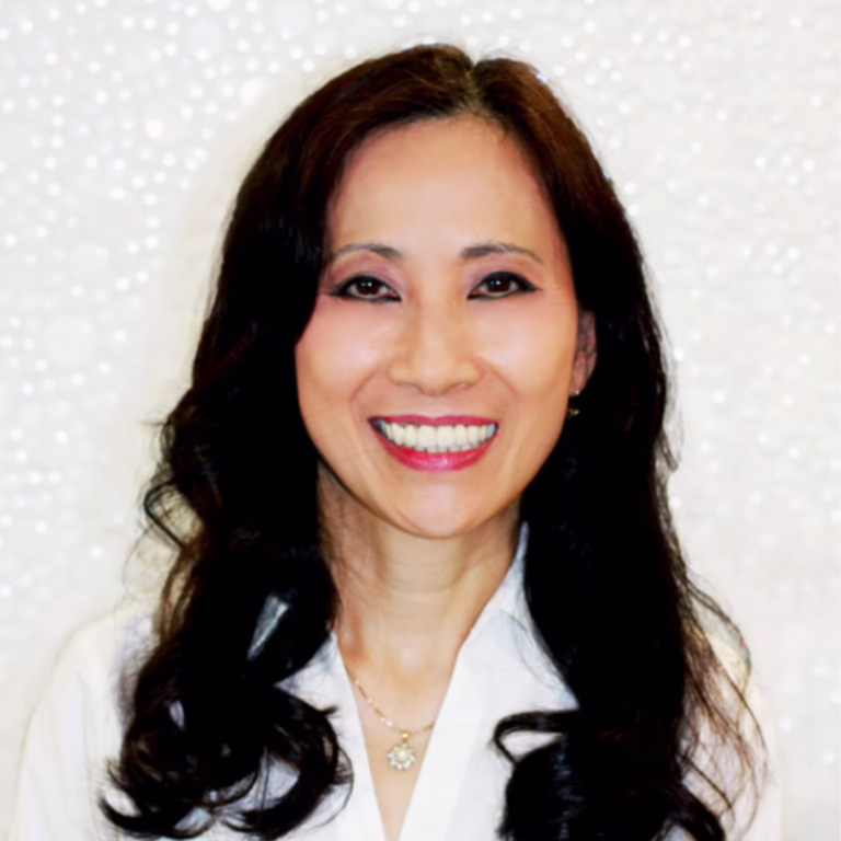 Smiling woman with long dark hair wearing a white blouse, posing against a sparkly backdrop.