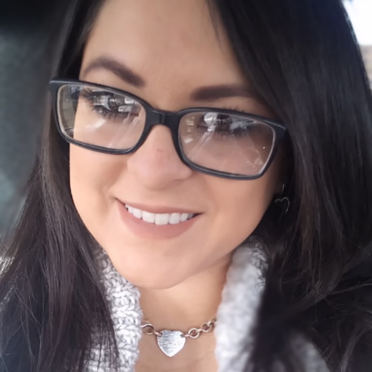 Smiling woman with long dark hair, black glasses, and a silver heart necklace.