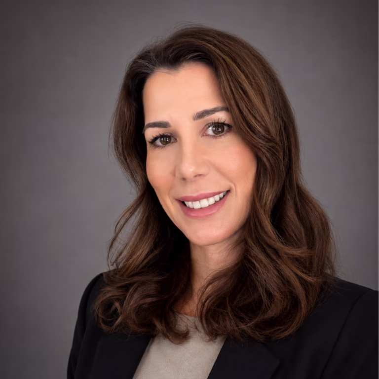 Professional headshot of a smiling woman with brown hair, wearing a black blazer against a gray studio backdrop.