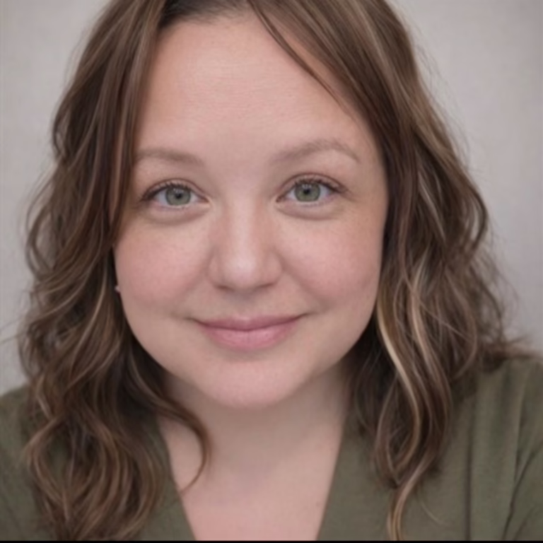 Close-up portrait of a smiling woman with wavy light brown hair, green eyes, and an olive-green top, neutral background.