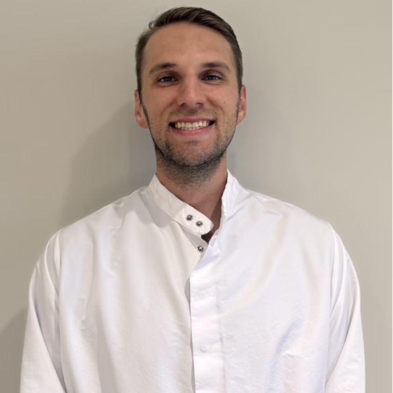 Portrait of a smiling man wearing a white lab coat against a light gray background.