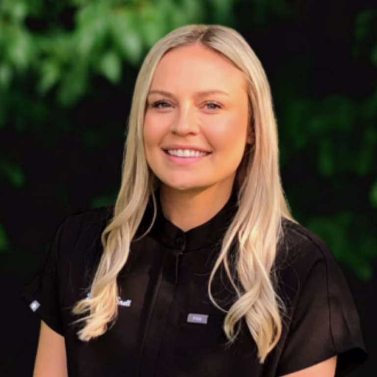 Portrait of a smiling blonde woman in a black uniform outdoors with greenery in the background.