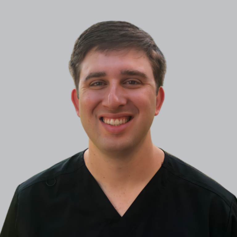 Smiling man in black scrubs against a light gray background, portrait view (healthcare professional)
