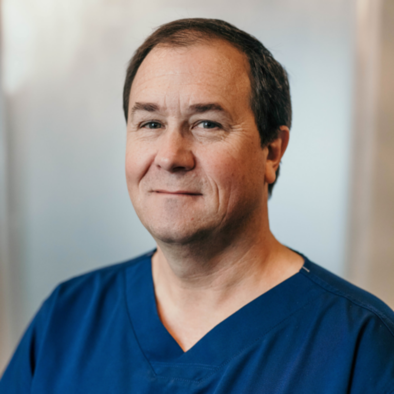 Portrait of a middle-aged man in blue scrubs smiling at the camera in a clinical setting