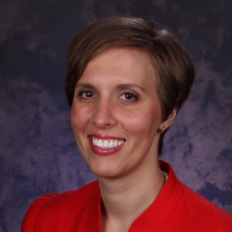 Professional headshot of a smiling woman with short brown hair wearing a red blouse.