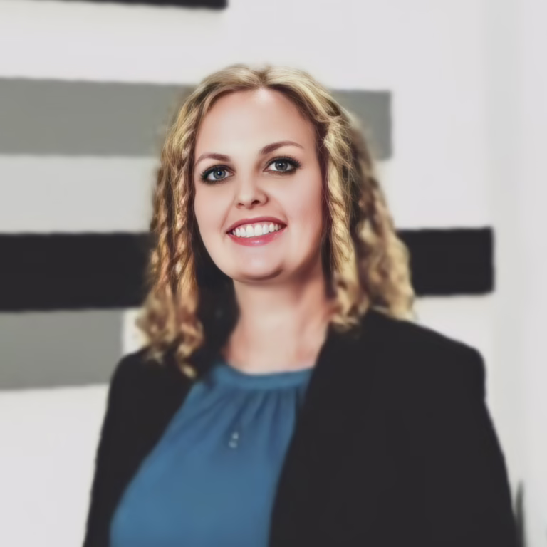 Professional woman with blonde wavy hair, wearing a teal blouse and black blazer, smiling at the camera with abstract wall art in the background.