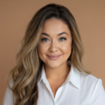 Portrait of a smiling woman with long wavy hair wearing a white collared shirt against a beige background.