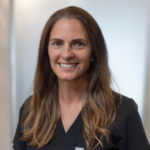 Smiling healthcare professional with long brown hair in black scrubs, portrait.