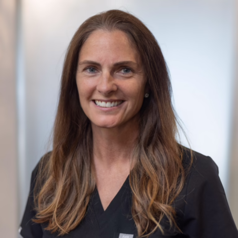 Smiling healthcare professional with long brown hair in black scrubs, portrait.