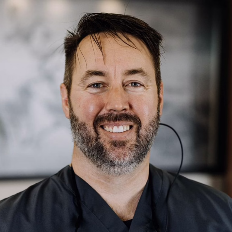 Smiling man with dark hair and beard wearing a black uniform and a headset microphone.