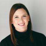 Portrait of a smiling woman with brown hair wearing a black turtleneck against a light gray background, looking at the camera.
