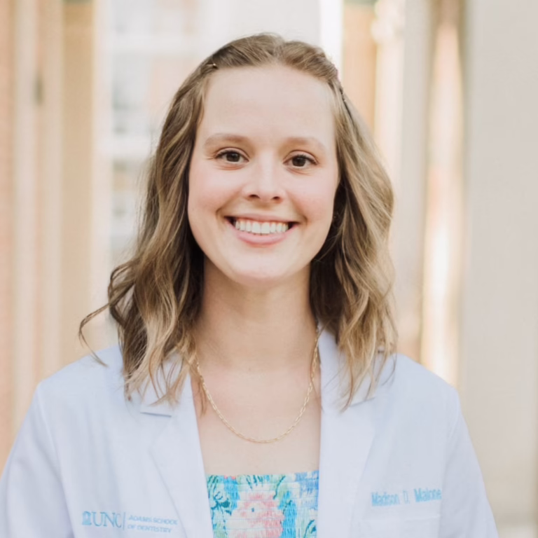 Portrait of a smiling woman in a light blue blazer and floral top, indoors, professional headshot.