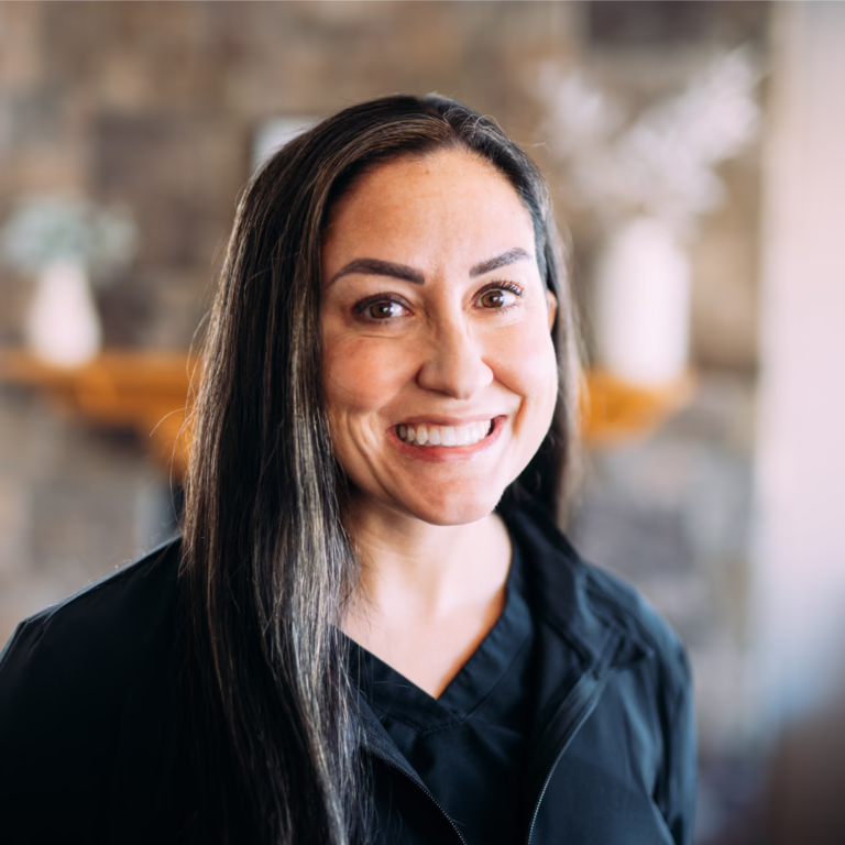 Portrait of a smiling woman with long dark hair, wearing a black jacket, indoors.