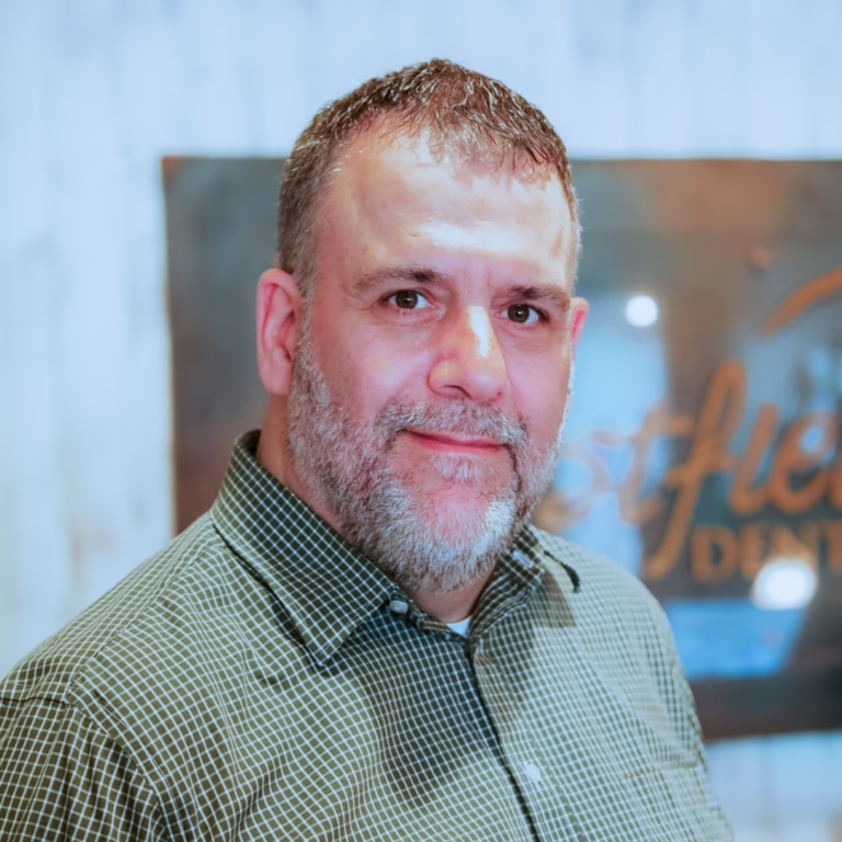 Portrait of a middle-aged man with short hair and a grey beard, wearing a green checkered shirt, looking at the camera.
