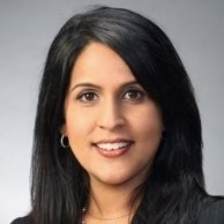 Head-and-shoulders portrait of a smiling woman with long black hair and hoop earrings against a gray background.