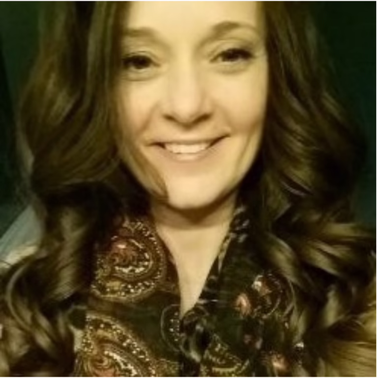 Close-up portrait of a smiling woman with wavy brown hair wearing a patterned paisley scarf in warm lighting.