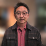 Portrait of a middle-aged man with glasses, short black hair, wearing a red shirt and dark jacket (head and shoulders).