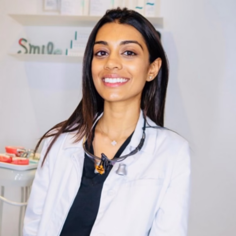 Smiling female healthcare professional in a white lab coat with a stethoscope around her neck in a clinical setting.