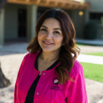Smiling woman in a bright pink jacket with a Campbell Dental Group logo outdoors.