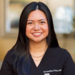 Portrait of a smiling female healthcare professional in black scrubs in a clinic setting.