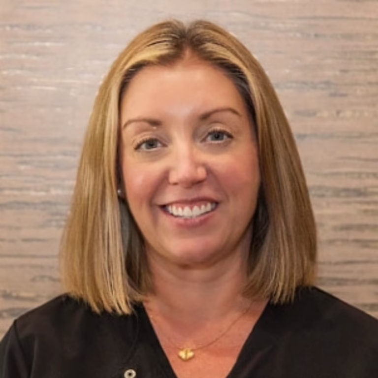 Head-and-shoulders portrait of a smiling woman with shoulder-length blonde hair, wearing a black top.