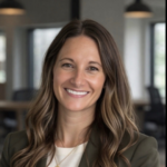 Smiling woman with wavy brown hair in a blazer, office background; friendly professional headshot.