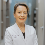 Portrait of a smiling female dentist in a white coat in a clinical hallway, ready to help patients.