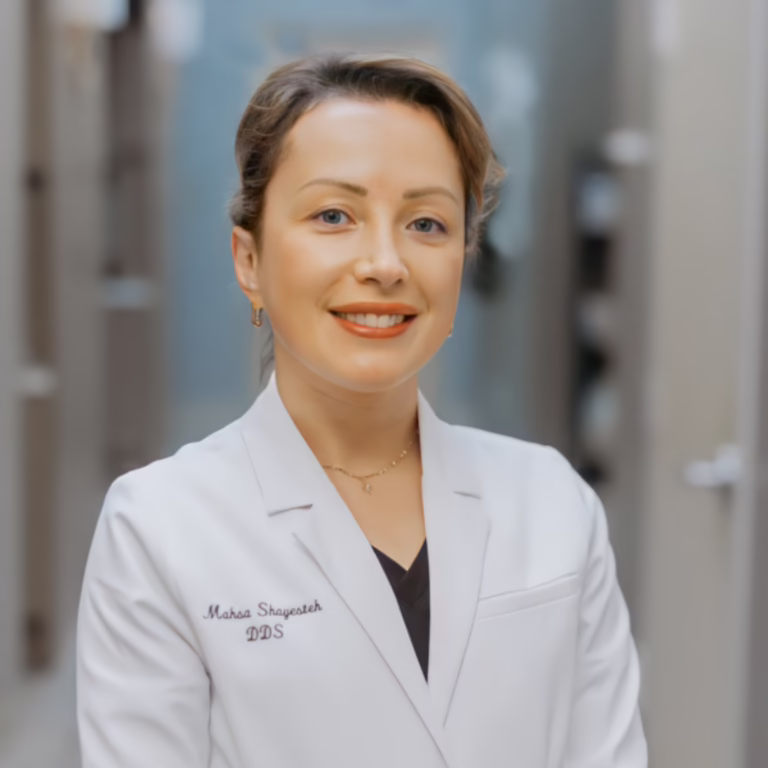 Portrait of a smiling female dentist in a white coat in a clinical hallway, ready to help patients.